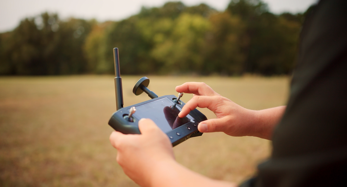 A man is holding a touch screen remote that controls a drone or UAV used for land surveying and mapping